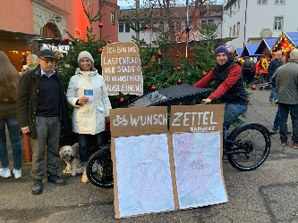 drei Personen mit einem Lastenfahrrad beim Weihnachtsmarkt, vor dem Rad steht ein großes Schild mit  der Aufschrift "Wunschzettel"