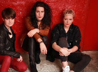 Die Band "Miss Foxy". Drei junge Frauen vor einer roten Wand.