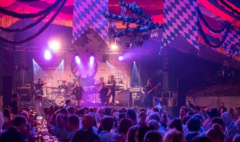 Bayrisch geschmütcktes Festzelt mit Band auf der Bühne und vielen Zuschauern.