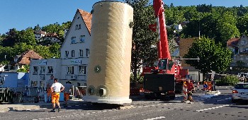 großes zylindrisches Bauteil hängt am Kran und wird von Kocherbrücke in die Baugrube gehoben.