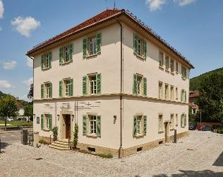 Blick auf ein historiches herrschaftliches Gebäude mit heller Fassade und grünen Klapläden