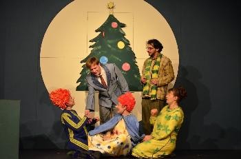 fünf Schauspielerinnen und Schauspieler stehen vor einem Bild eines Weihnachtsbaum.