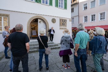 Stadtführer steht auf einem kleinen Treppenpodest vor der Eingangstüre des Alten Rathauses und erläutert Zuhörenden
