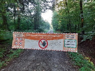 Banner mit Warnhinweis und Durchfahrtsverbot über einen Waldweg gespannt.