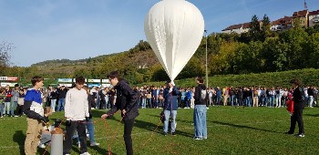 weißer Ballon steht über einer Menschengruppe auf dem Sportplatzrasen, blauer Himmel