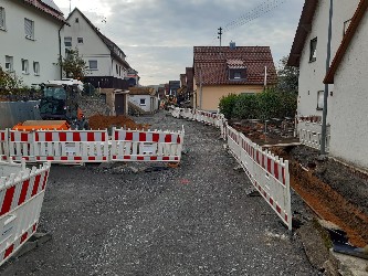 Baustelle in einer engen Straße, die aufgerissen und behelfsmäßig mit Schotter geschlossen ist.