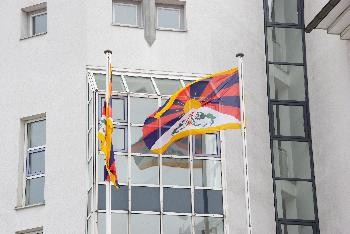 Blick auf zwei Tibetfahnen, die außen an der weißen Rathausfassade wehen