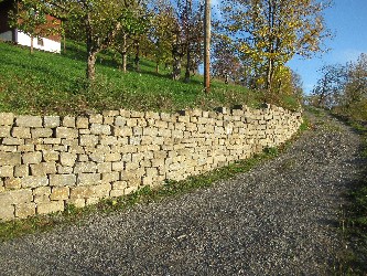 ansteigender Feldweg der links durch eine neu aufgesetzte Trockenmauer begrenzt ist. oberhalb der Mauer ist eine Streuobstwiese z s