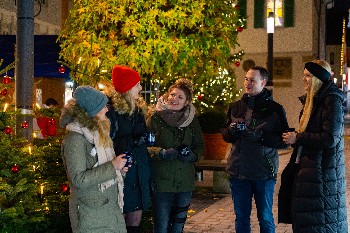 vier junge Frauen und ein junger Mann in Winterkleider vor dem Christbaum am  Alten Rathaus mit Tassen in der Hand