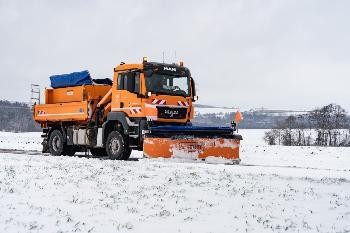 großes orangefarbenes Räumfahrzeug mit herabgelassenem Schneepflug in einer verschneiten Landschaft