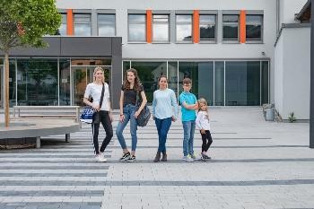 fünf Kinder stehen nebeneinander vor einem Schulgebäude