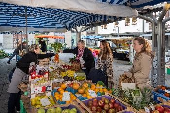 Marktstand mit Obst inder Auslage, drei Frauen werden von einer Markthänderlin bedient