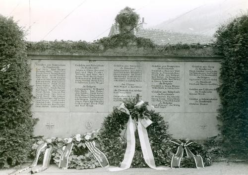 Blumenkränze vor einem Gedenkstein.