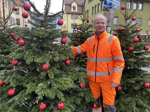 Müllmann neben dekorierten Christbäumen.