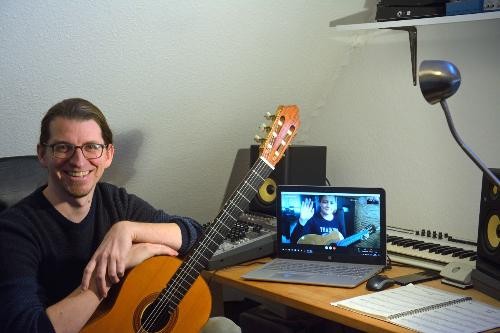 Gitarrenlehrer Ralph Hanl mit Giarre in der Hand, im Hintergrund ein Laptop für den Online-Unterrict.