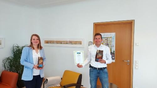 Bürgermeister Neumann und Mitarbeiterin mit Fairtrade-Urkunde und Kaffee in der Hand.