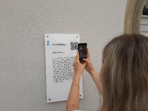 Smartphone scannt einen QR-Code an einer historischen Tafel ab.
