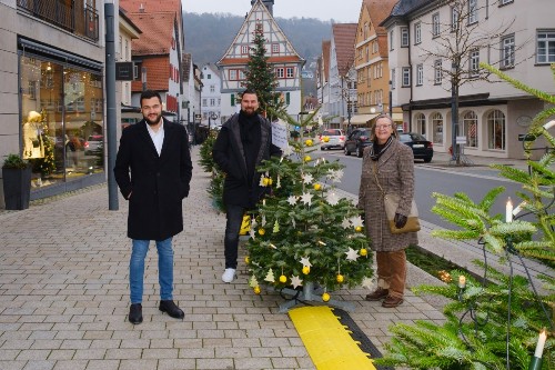 Drei Personen stehen an einem dekorierten Weihnachtsbaum in der Künzelsauer Hauptstraße.