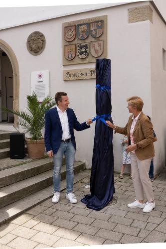 Bürgermeister Stefan Neumann und Ehrenbürgerin Ursula Berner enthüllen eine blau eingühllte  Stele