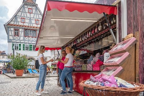 drei Frauen vor einem Marktstand mit textilen Angeboten, im Hintergrund das Alte Rathaus.