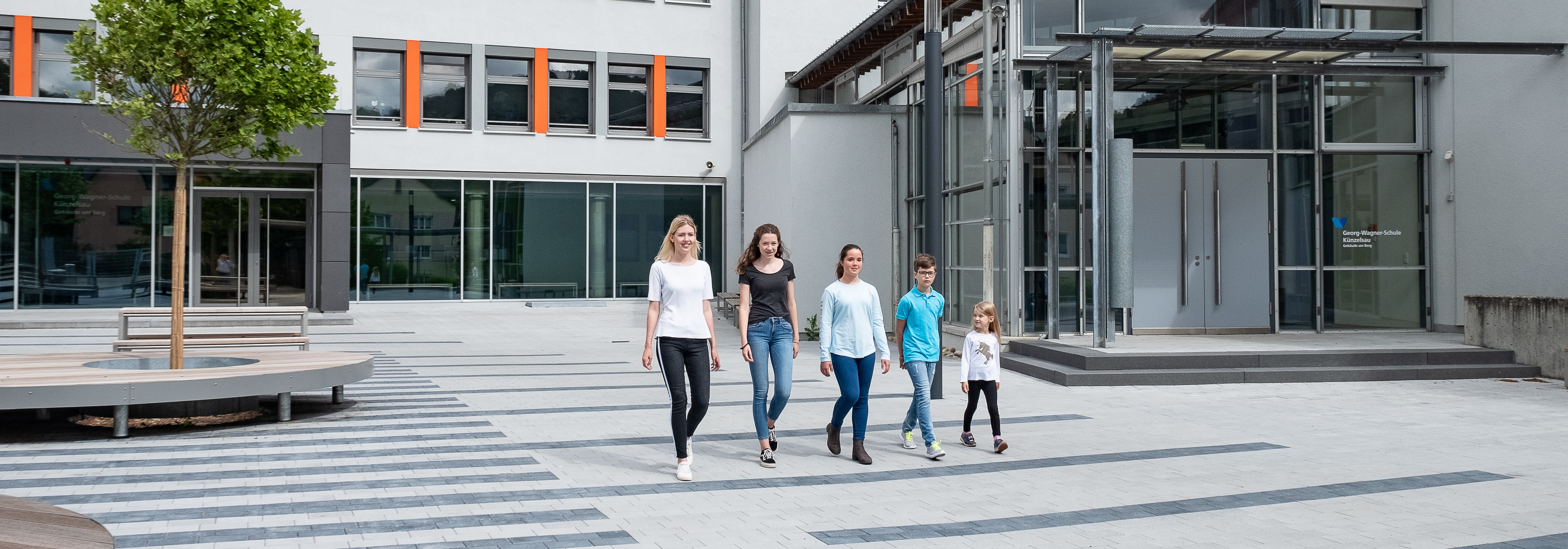 Fünf Schüler laufen über einen Schulhof.
